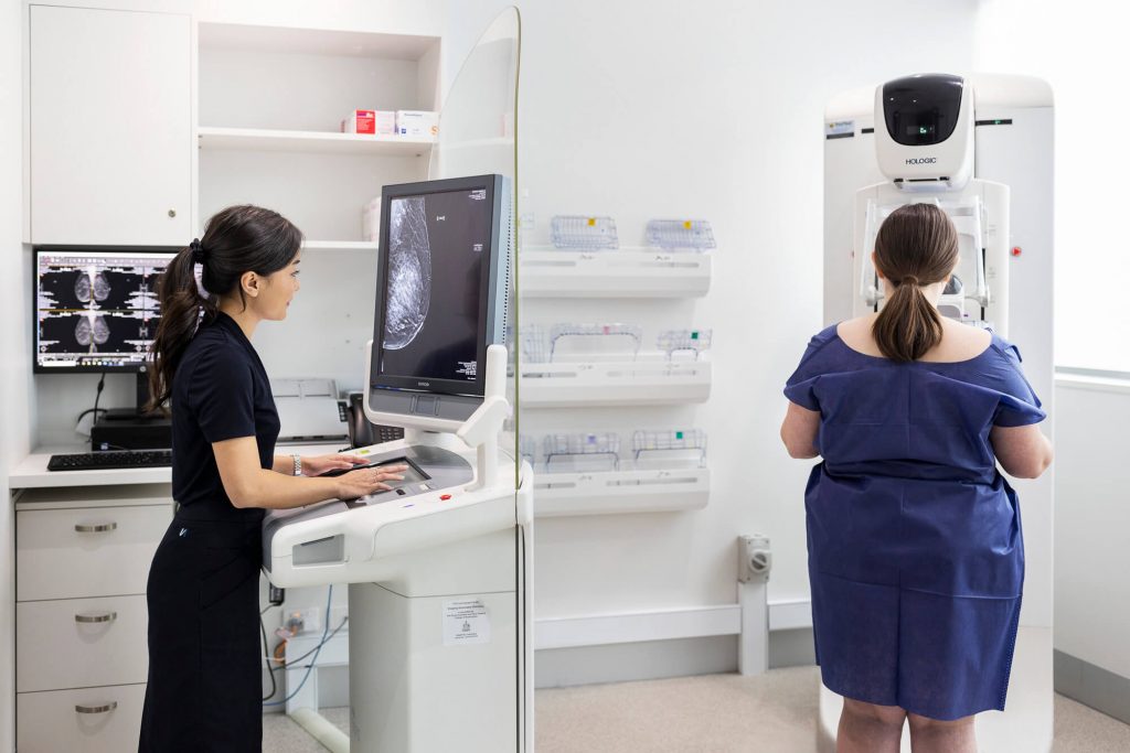 A mammographer using 3D mammogram equipment to scan a female patient.